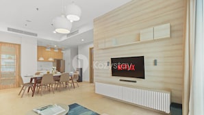 Een moderne woonkamer met een grote flatscreen televisie bevestigd aan een houten wand, een eethoek met een houten tafel en stoelen, en hanglampen.