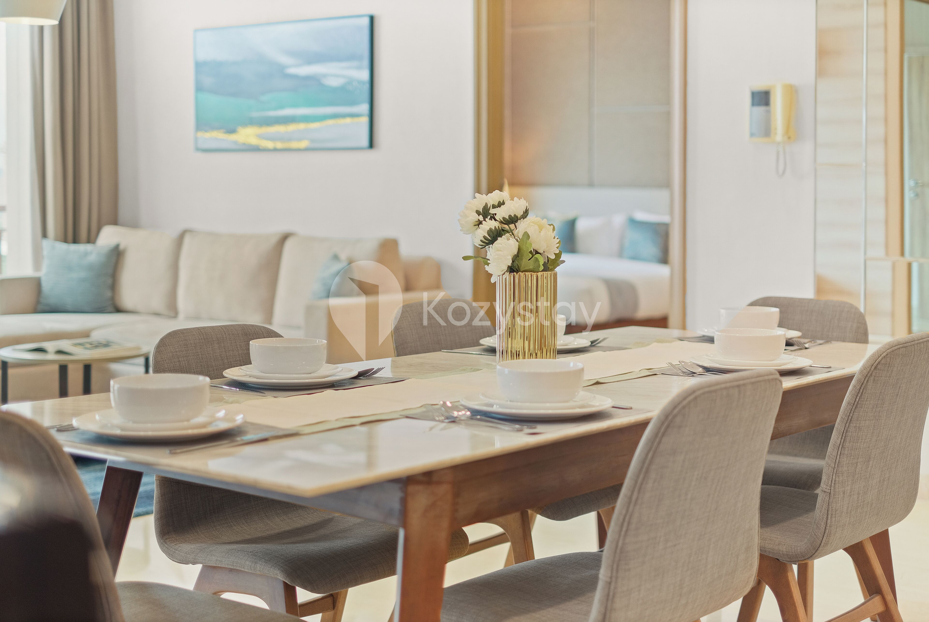 A dining area with a table set for four, a vase with flowers, and a painting on the wall.