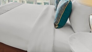 Een net opgemaakt bed met witte lakens en een blauwgroen kussen.