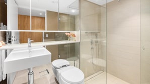 Un baño moderno con cabina de ducha de vidrio, un lavamanos blanco y un inodoro.