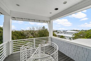 A covered outdoor balcony with a white railing, a circular white bench, and a view of houses and trees. - 30A Beach House - Dream by the Sea  (Santa Rosa Beach)