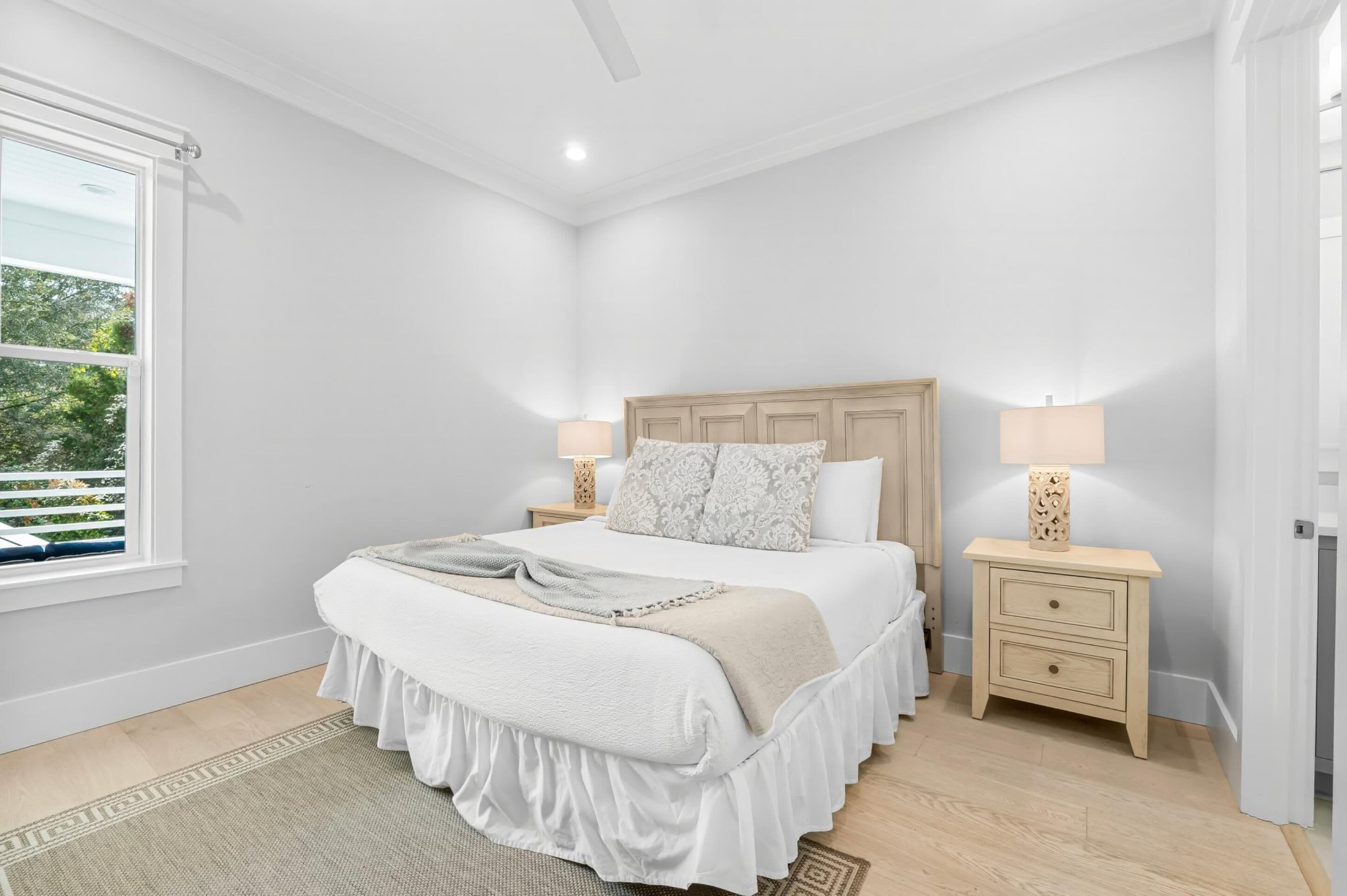 A bedroom with a bed, two bedside tables, a window, and a door.