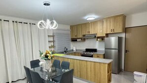 Une cuisine moderne avec des meubles en bois, un réfrigérateur en acier inoxydable, une cuisinière à gaz et un coin repas comprenant une table et des chaises en verre.