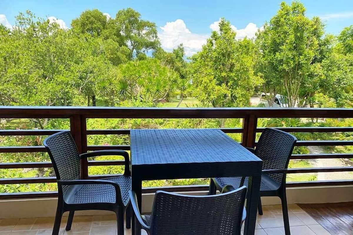 A balcony with a table and chairs, overlooking a lush green landscape with trees and a clear sky.