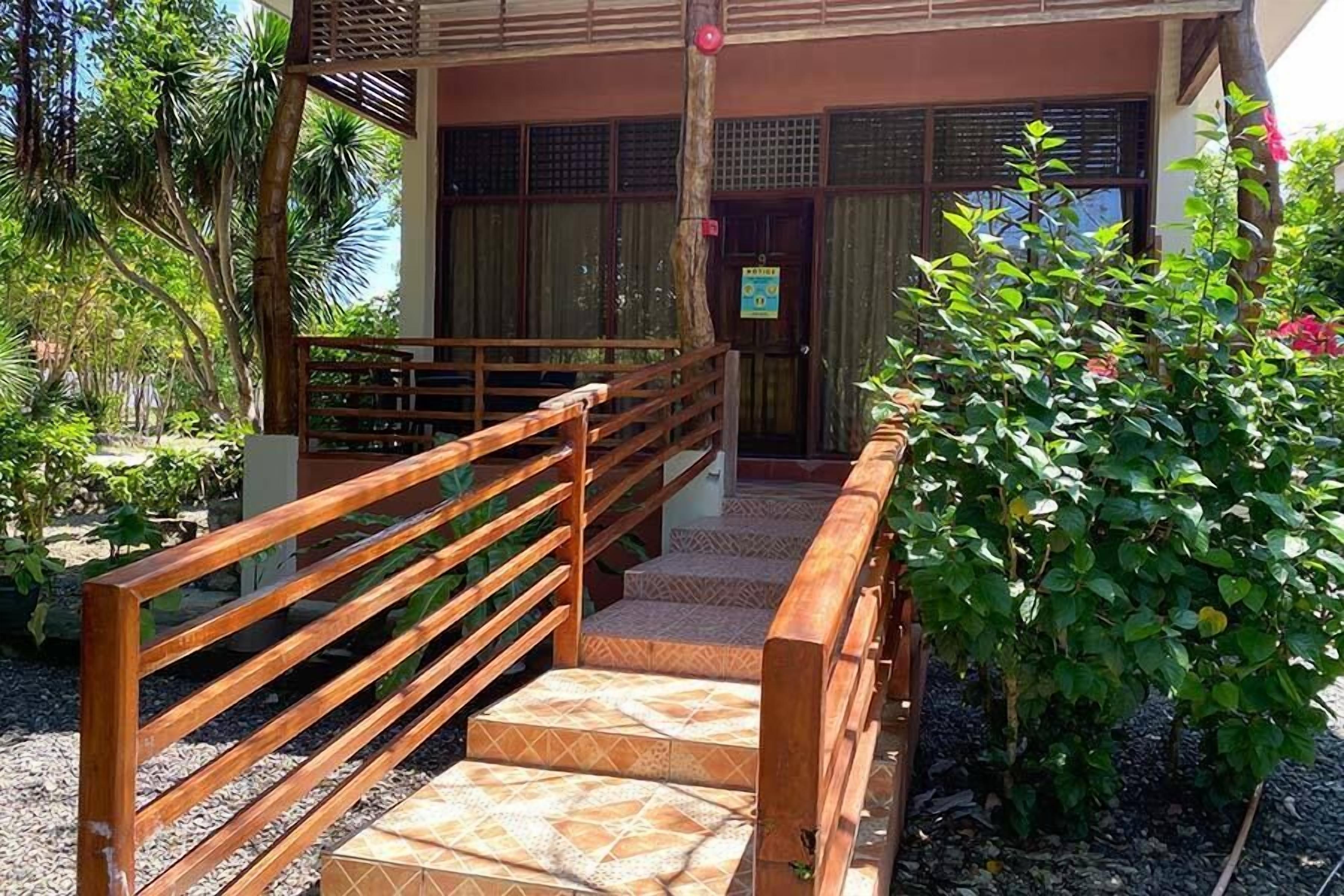 A wooden staircase leading to a building with a traditional design, surrounded by greenery and a small garden area.