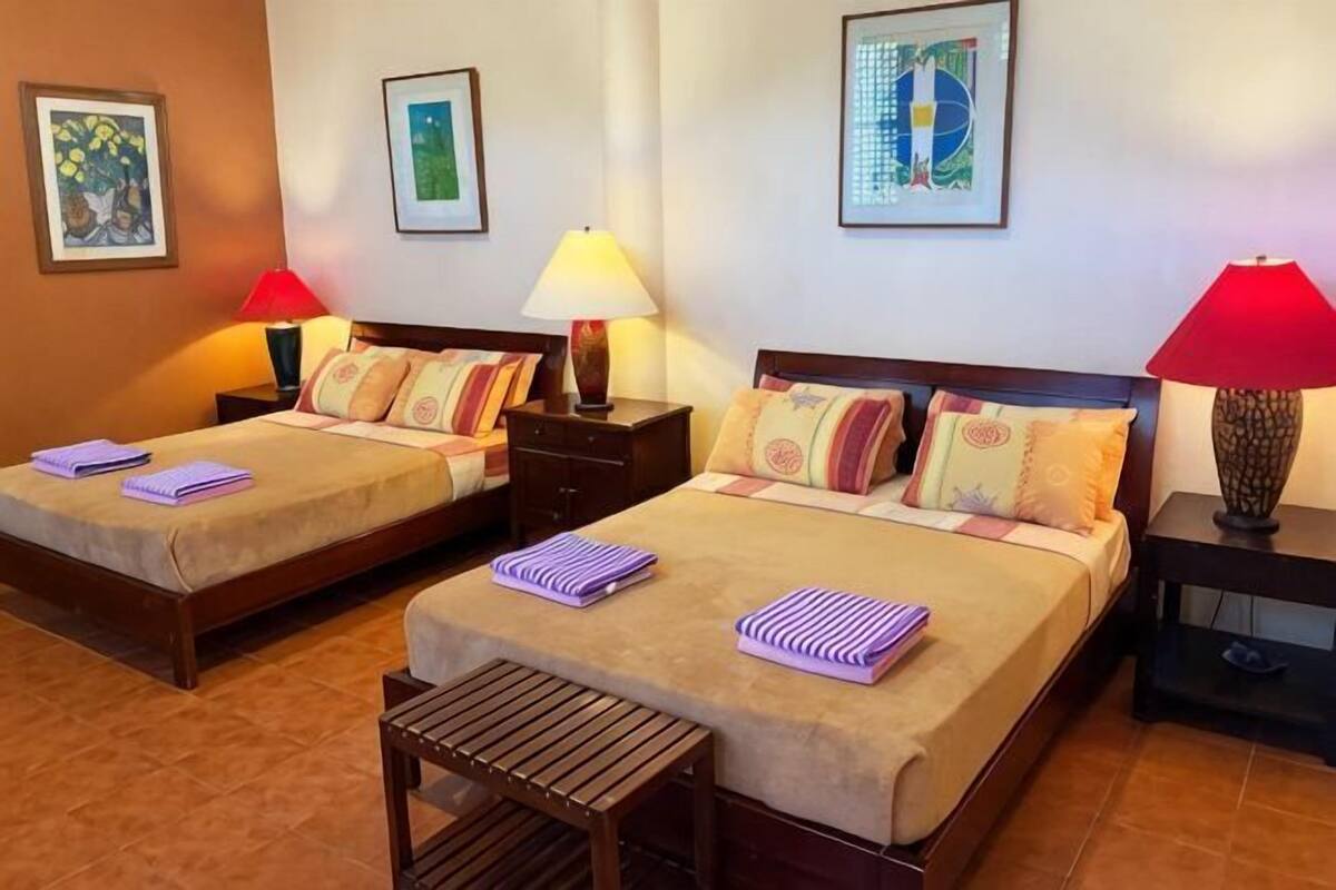 A hotel room with two beds, each with a nightstand, a lamp, and a small table.