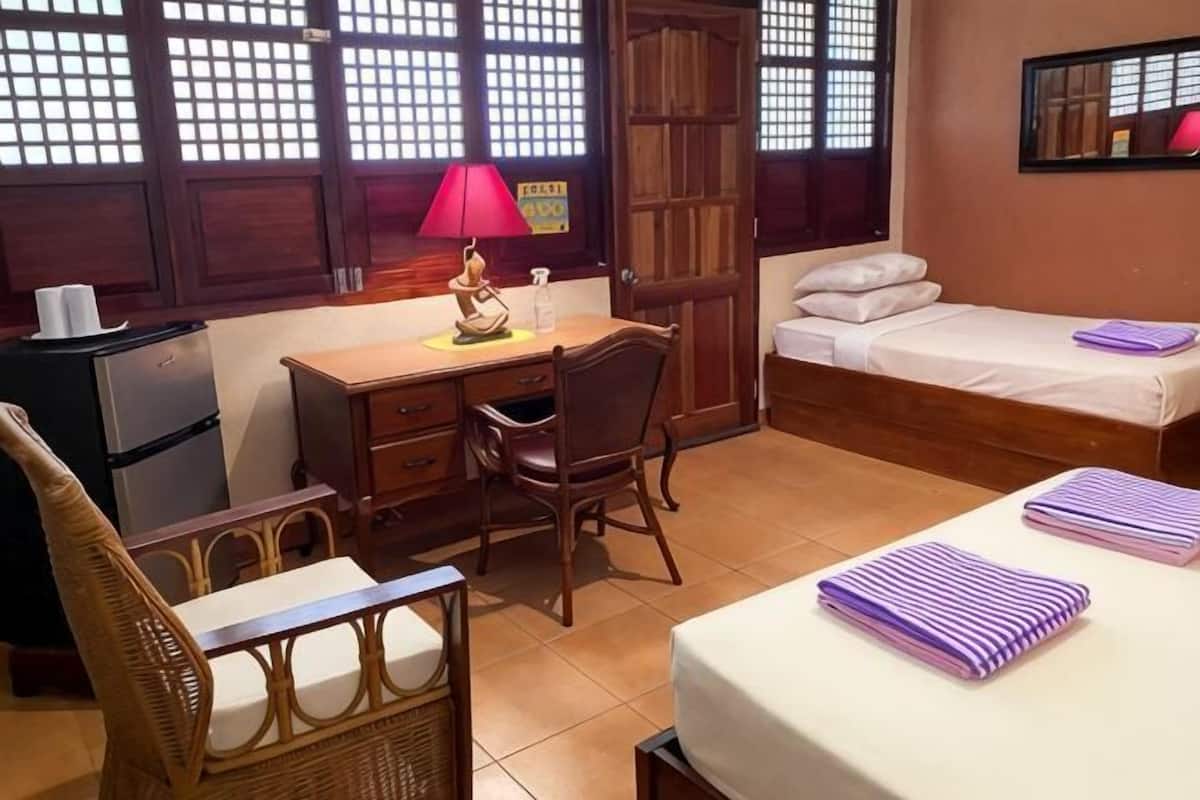 A room with a desk, chair, bed, and a small kitchenette.