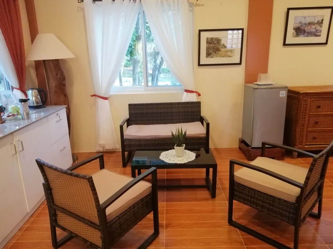 A cozy living area with a sofa, two chairs, a coffee table, a TV, and a window with curtains.