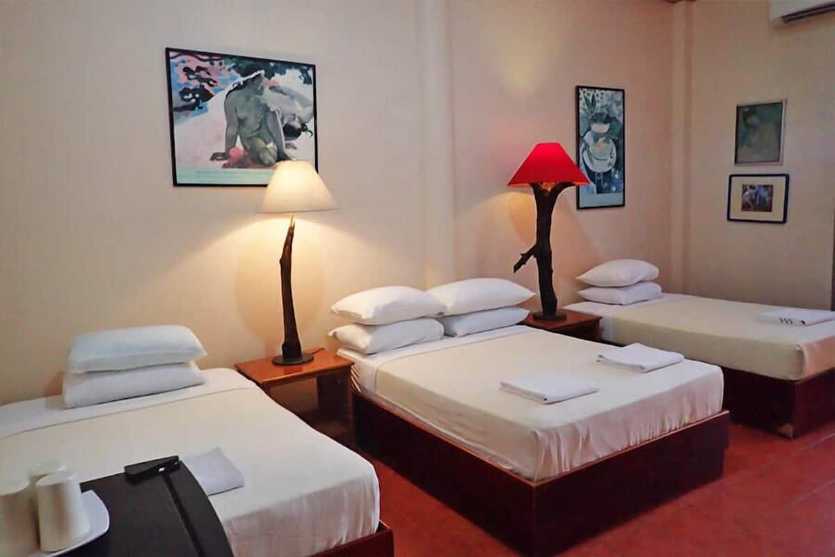 A hotel room with two single beds, each with white linens and pillows, a nightstand with a lamp, and a wall-mounted painting.