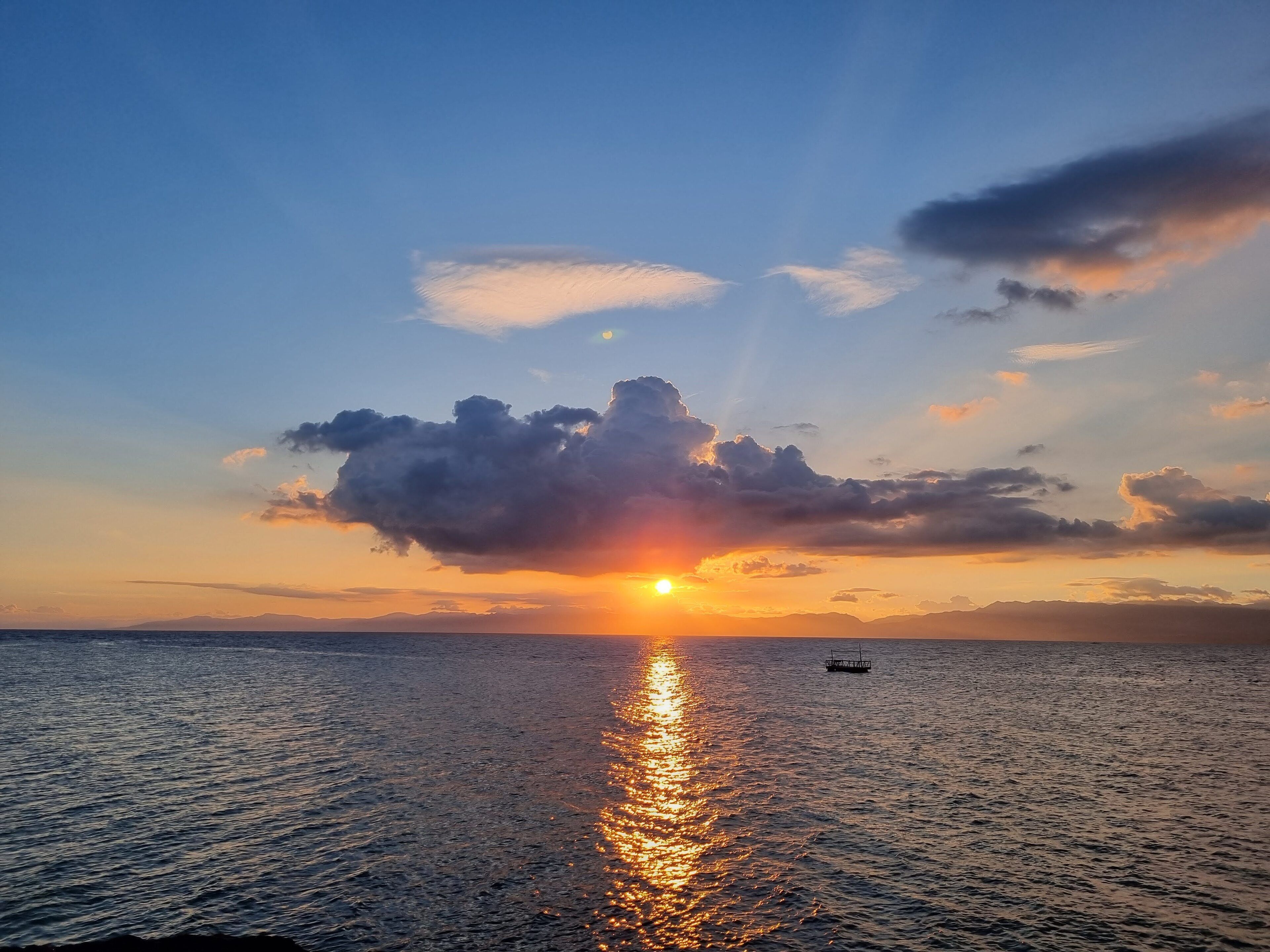 A sunset over a calm sea with a boat in the distance.