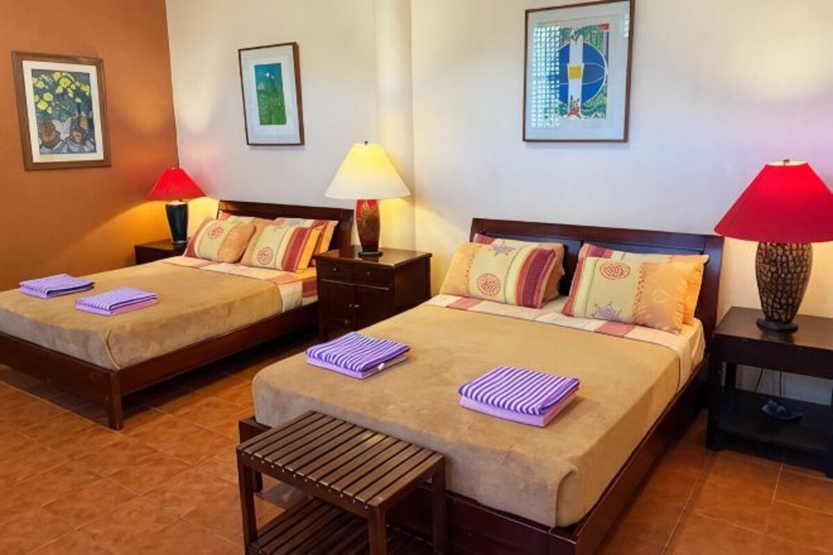 Habitación de hotel con dos camas, cada una con una mesita de noche, una lámpara y una pequeña mesa.