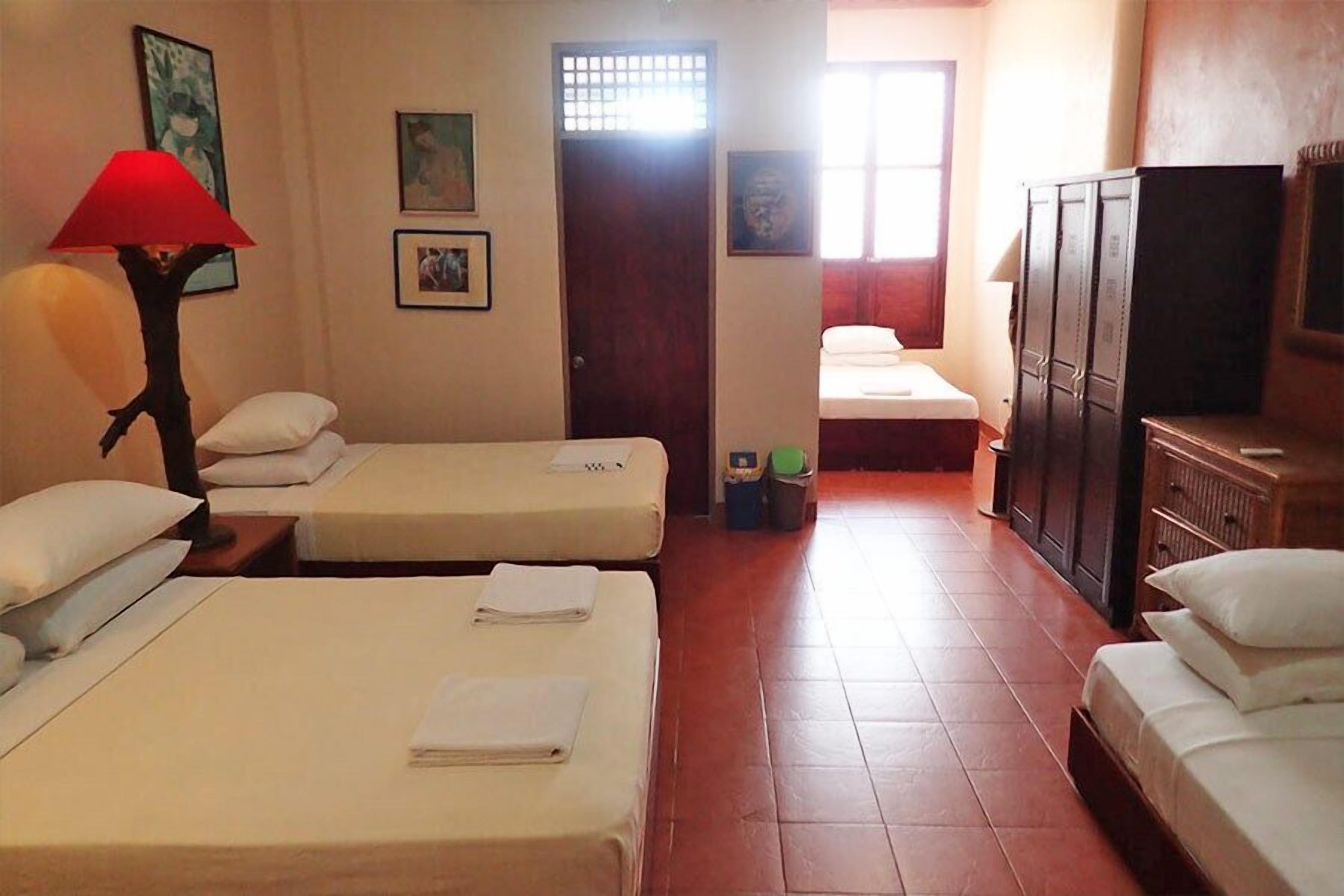Quarto de hotel com duas camas, televisão, guarda-roupa e janela com cortinas.