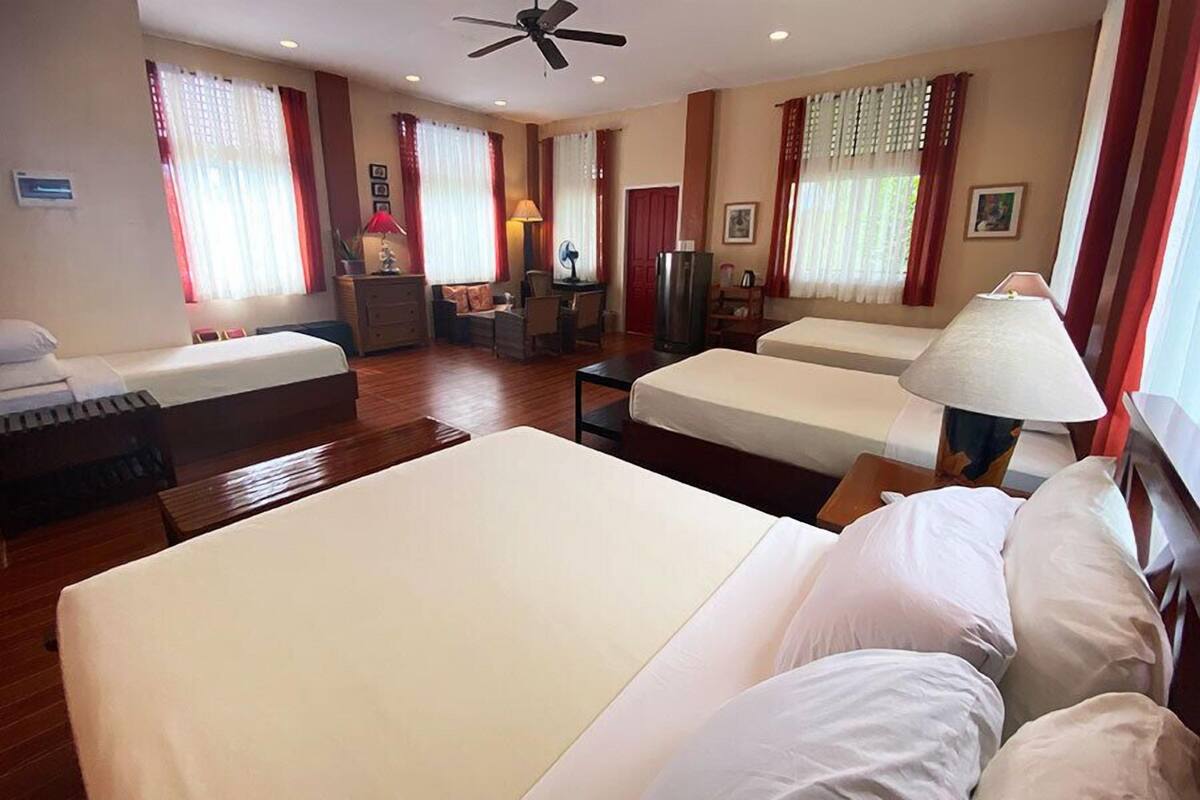 A hotel room with two beds, a desk, a chair, a lamp, and a ceiling fan.