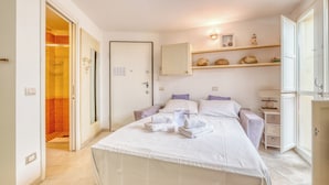A bedroom with a bed, a nightstand, a wardrobe, and a shelf with decorative items.