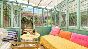 A conservatory with a bed, a table with a bottle and glasses, and a fan.