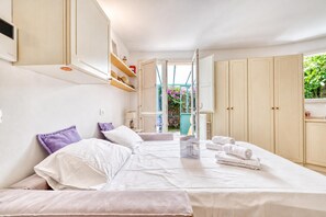 A bedroom with a bed, pillows, a nightstand, a wardrobe, and a window with a view of greenery. - Nice Studio With Garden and Terrace, Menton, France (Menton)
