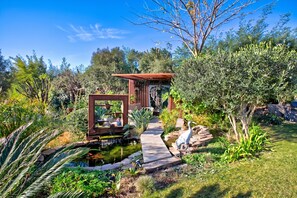 A garden with a pond, a wooden walkway, and a pergola structure.