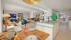 Una cocina moderna con una isla central, un comedor con mesa de madera para cuatro personas y una sala de estar con sofá y televisor.
