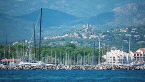 Una marina con barcos amarrados, un rompeolas rocoso y un pueblo con edificios al fondo.