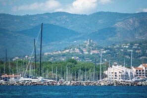 A marina with boats docked, a rocky breakwater, and a town with buildings in the background. - Villa Bayugita, Grimaud, France (Grimaud)