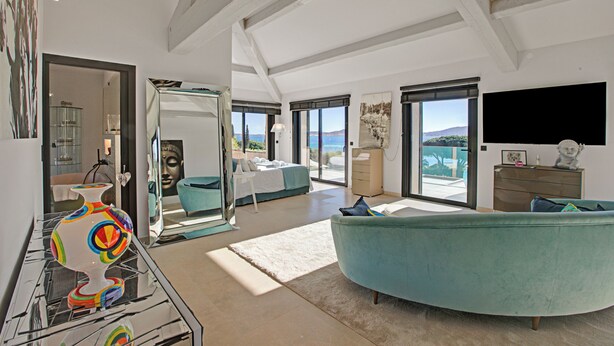 A spacious living area with a curved teal sofa, a glass coffee table, and a large window offering a view of the sea. - Villa Bayugita With Master Bedroom, Grimaud, France (Grimaud)