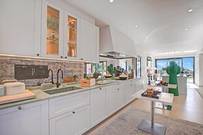 Une cuisine moderne avec des meubles blancs, un pare-feu en marbre et une vue sur l’extérieur.