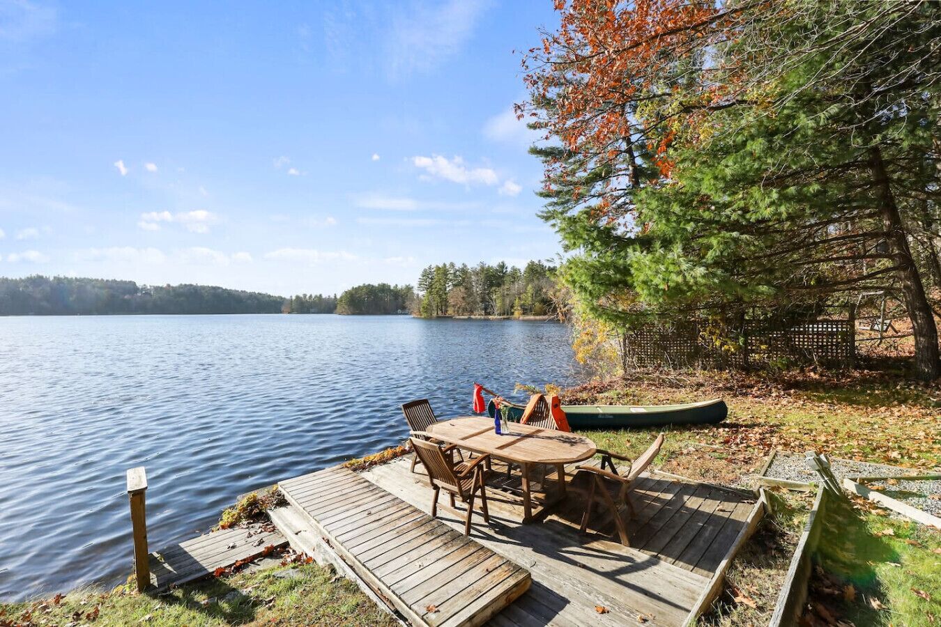 A lakeside deck with a table and chairs, a canoe, and a wooden fence.