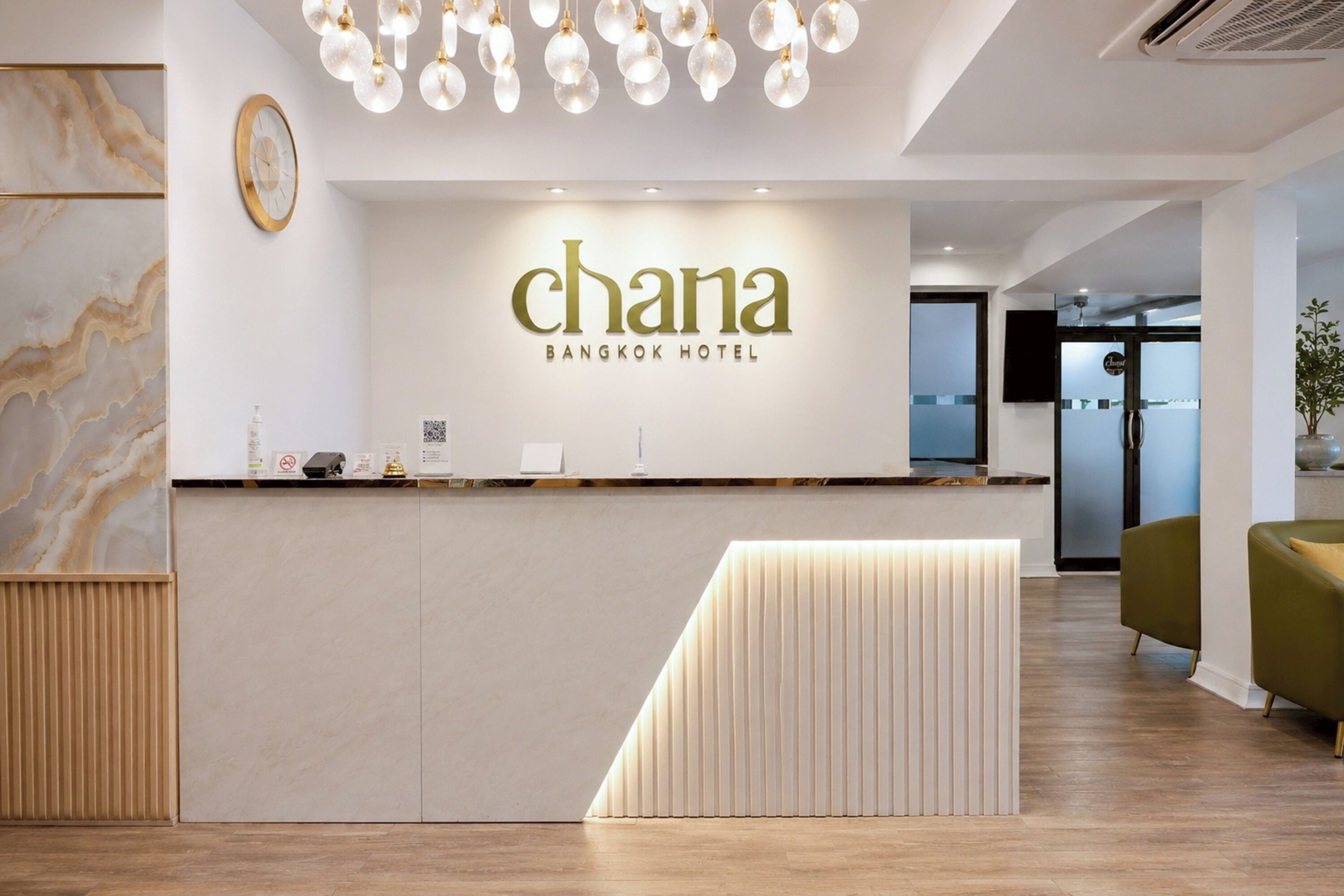 Een modern ontworpen receptiebalie, een klok en een bordje met 'Chana Bangkok Hotel'.
