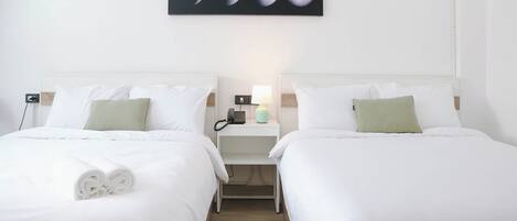 A hotel room with two beds, white bedding, a nightstand with a lamp, and a wall-mounted picture of the moon phases.