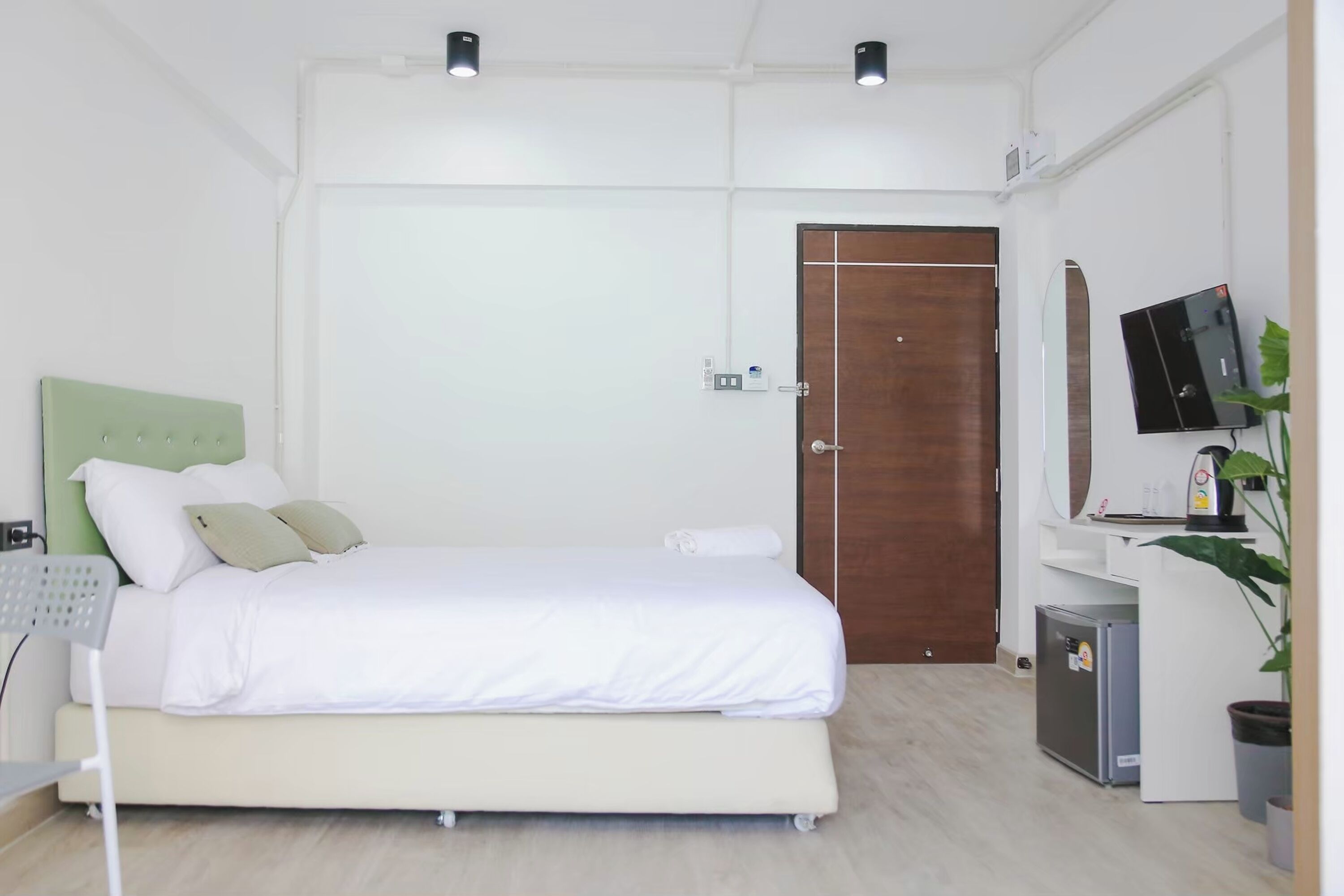 A bedroom with a bed, a desk, a television, and a door.