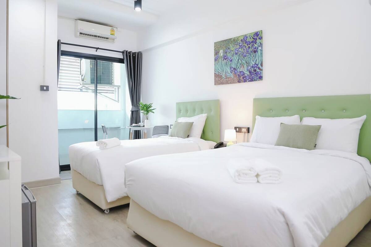 Een hotelkamer met twee bedden, een balkon en een groen hoofdeinde.