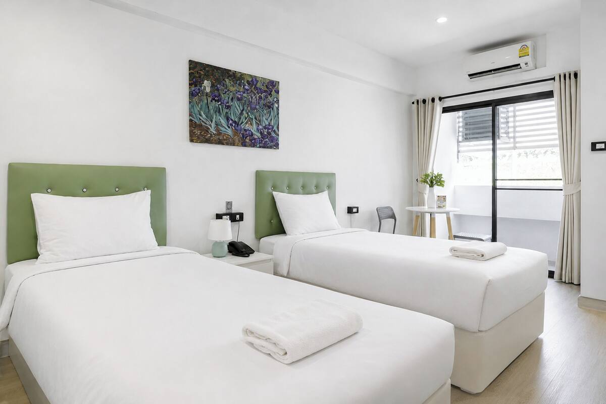 Een hotelkamer met twee bedden, een schilderij, een klein tafeltje met een plant en een airconditioning.