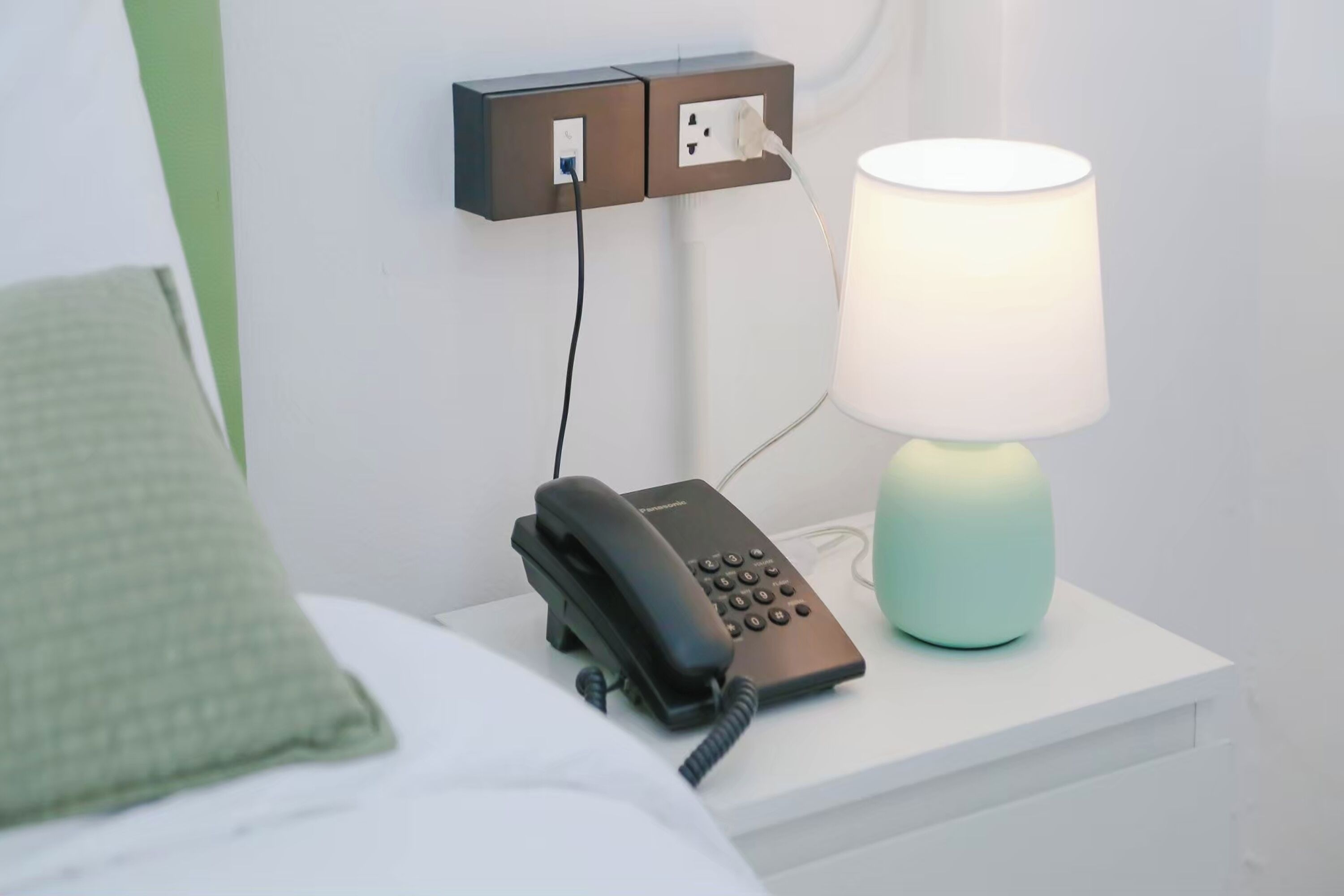 A bedside table with a black telephone, a lamp, and a power outlet.