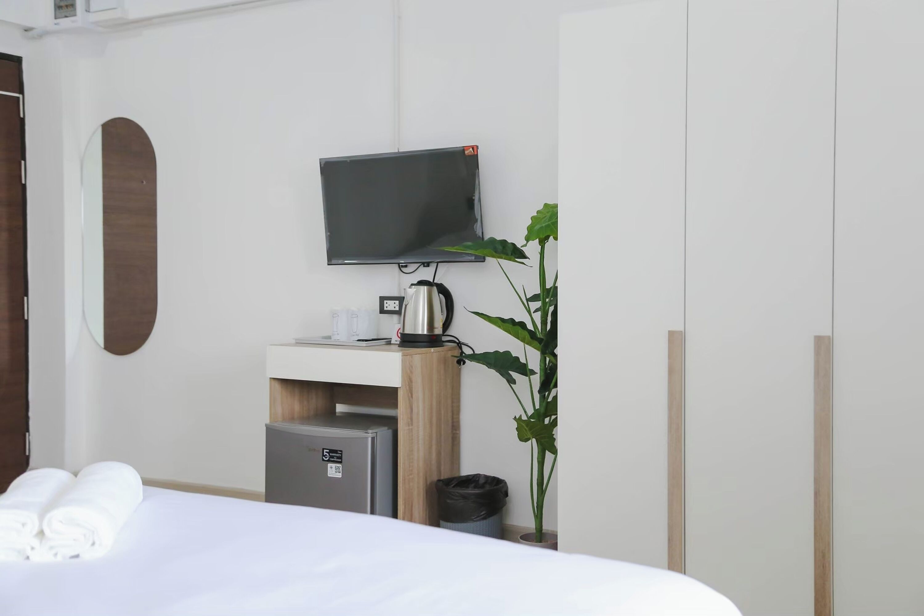 Ein Hotelzimmer mit Bett, Flachbildfernseher an der Wand, einer kleinen Küchenzeile inklusive Kaffeemaschine, Mülleimer und einer Topfpflanze.