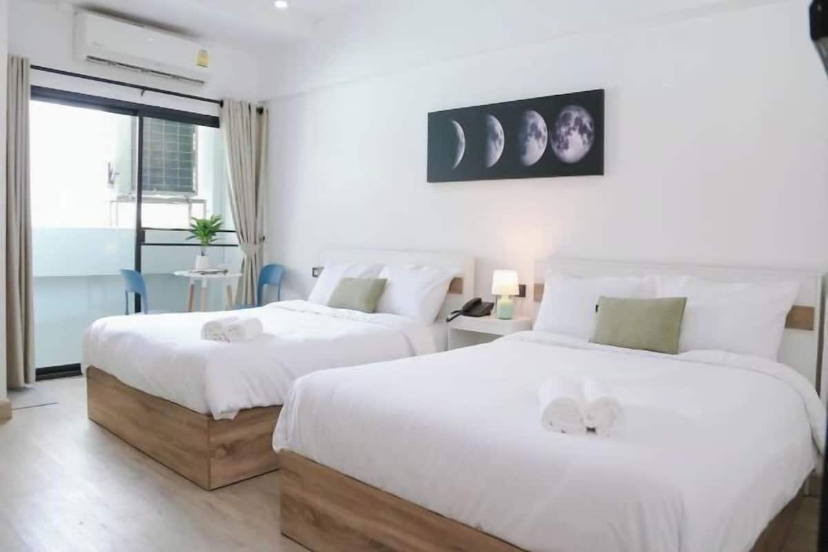 Hotelkamer met twee bedden, een balkon met uitzicht, een schilderij van de maanstanden en een tafeltje met een plant.