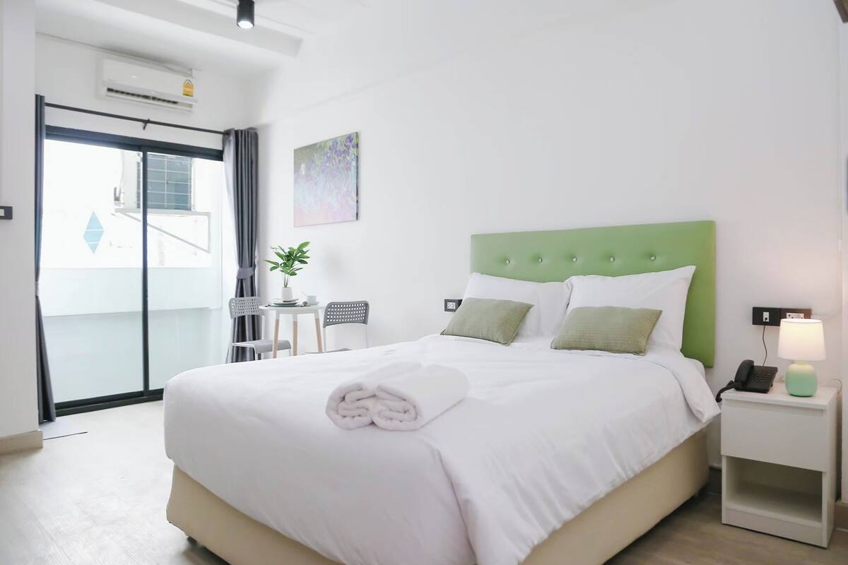 Een hotelkamer met een bed, een nachtkastje met een lamp, een stoel, een kleine tafel en een potplant.