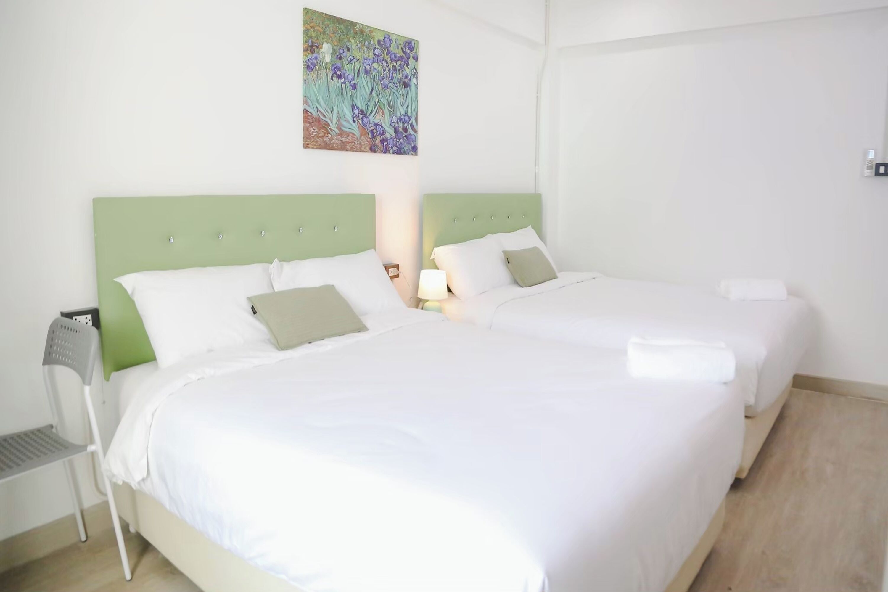 A hotel room with two beds, each with white bedding and green headboards. There is a painting on the wall above the beds.