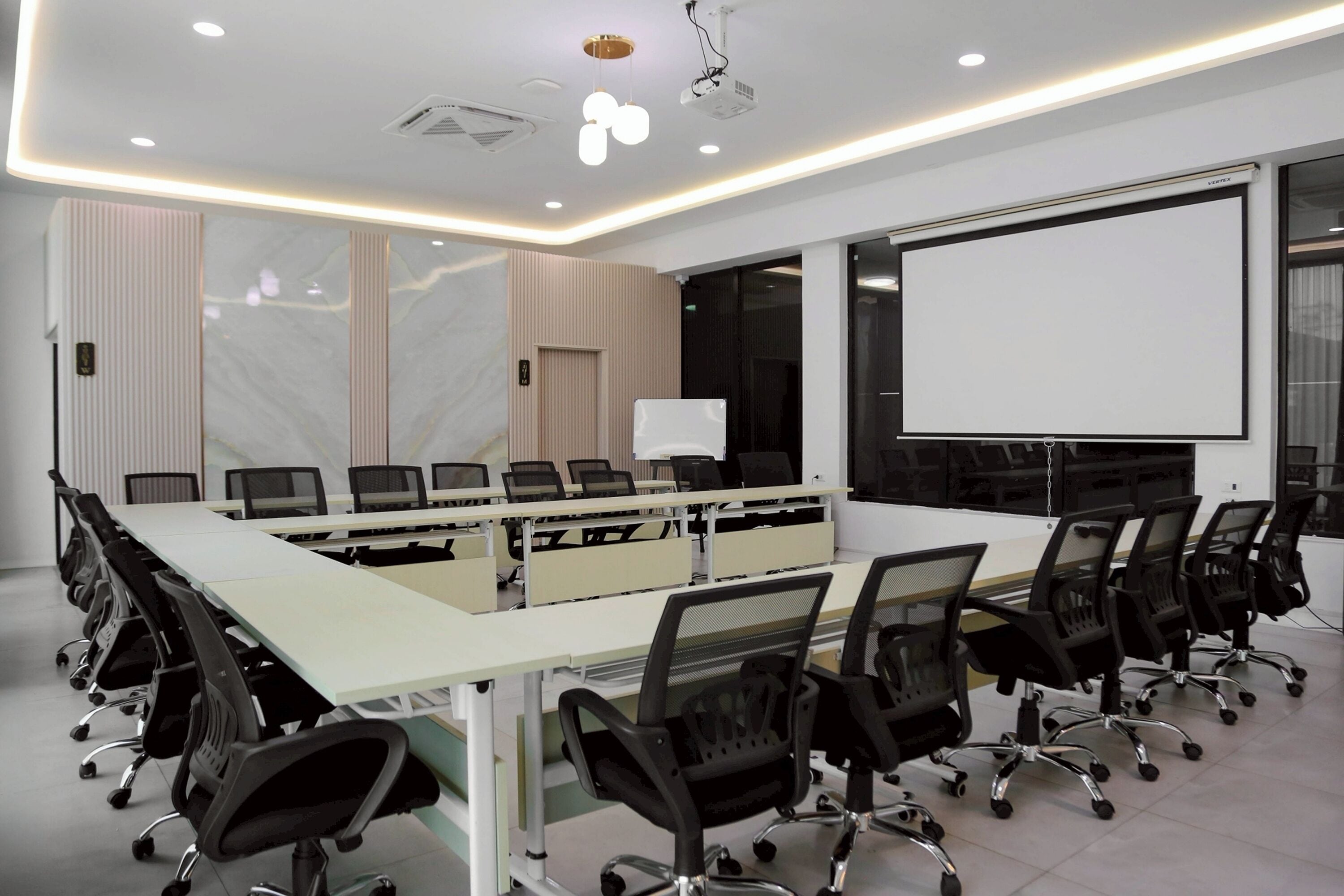 A conference room with a long table, chairs, a projector screen, and a whiteboard.