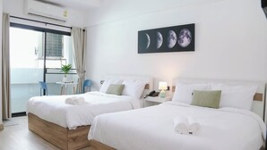 A hotel room with two beds, a small table with a plant, and a window with curtains. - Chana Bangkok Hotel (Bangkok)