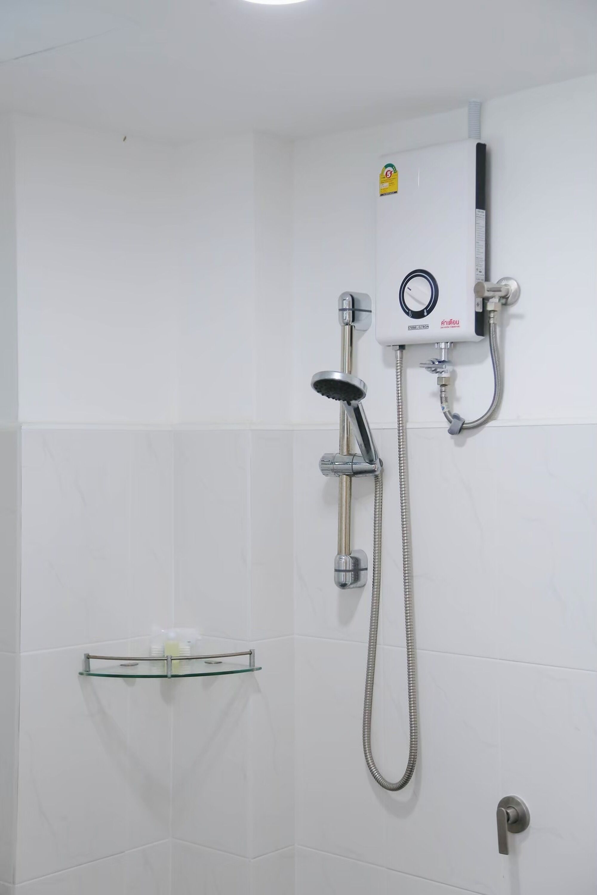 A bathroom with a shower, a glass shelf, and a wall-mounted control panel.