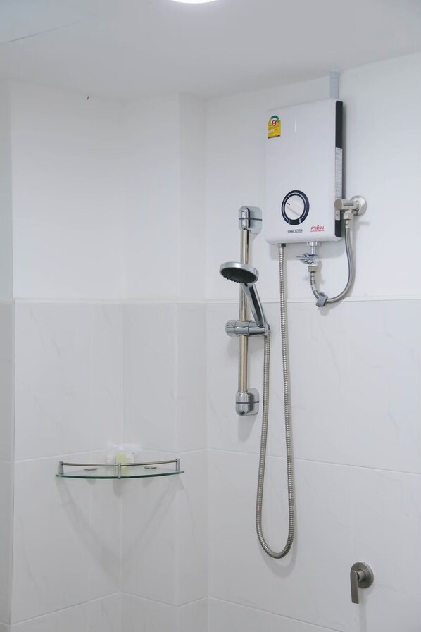 Un baño con ducha, repisa de vidrio y panel de control en la pared.