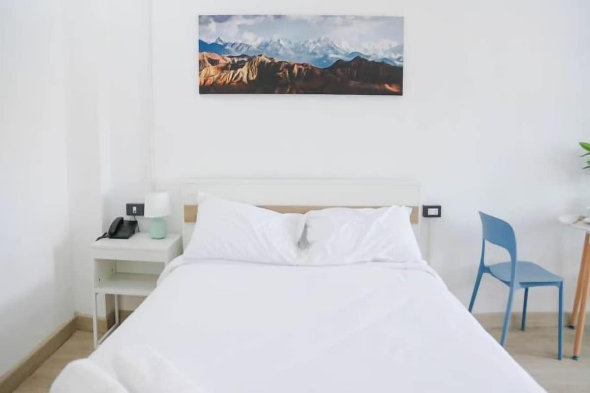 Une chambre d’hôtel avec un lit, un bureau avec un téléphone, une chaise et un tableau représentant des montagnes accroché au mur.