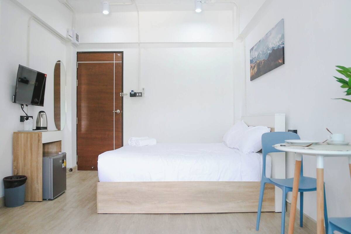 Een hotelkamer met een bed, een bureau met stoel, een televisie, een kleine koelkast en een prullenbak.