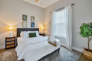 Un dormitorio con cama, dos mesitas de noche con lámparas, una ventana con persianas y decoración en la pared.