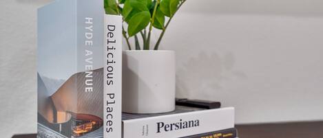 A stack of books titled 'Hyde Avenue', 'Persiana', and 'The Complete Illustrated Guide to Feng Shui' on a wooden surface with a potted plant in the background.