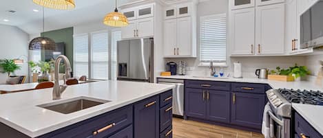 Una cocina moderna con armarios blancos, bajos en color azul oscuro, un refrigerador de acero inoxidable y una estufa a gas.
