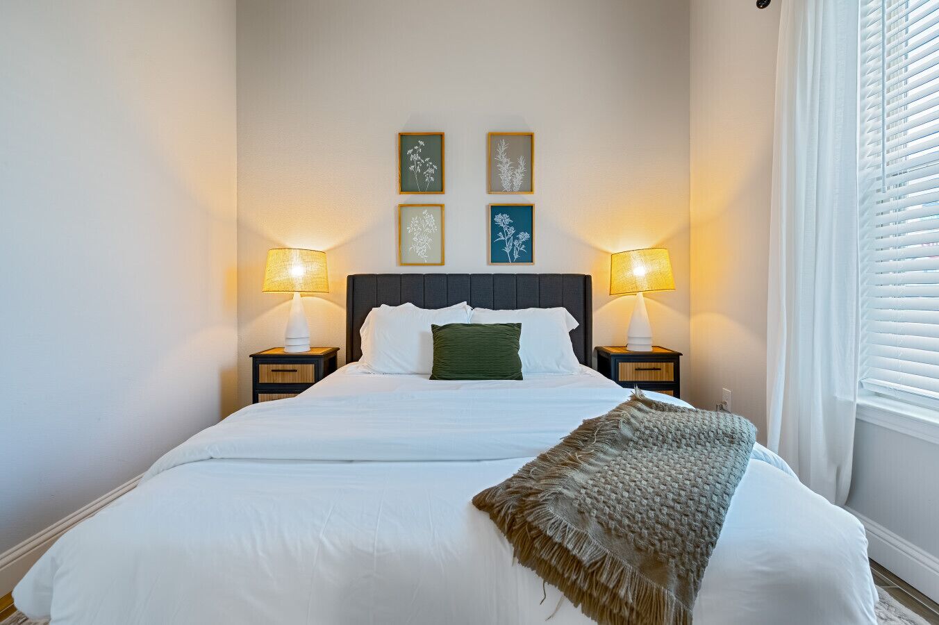 Una cama bien hecha con sábanas blancas, dos lámparas de noche y un plaid decorativo.