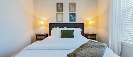Una cama bien hecha con sábanas blancas, dos lámparas de noche y un plaid decorativo.