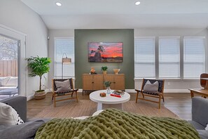 A modern living room with a large window, a dining area, and a cozy seating arrangement.
