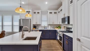 Une cuisine moderne avec des meubles blancs, un îlot central, des appareils en acier inoxydable et des luminaires suspendus.